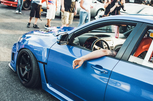 Attendee leaning out the window of a blue sports car at the car meet