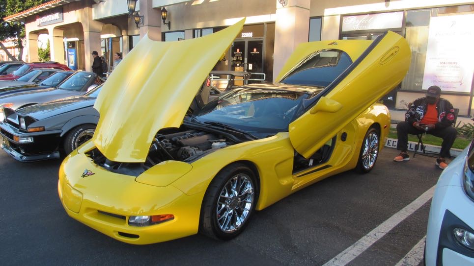 Yellow Corvette with vertical doors and hood open on display